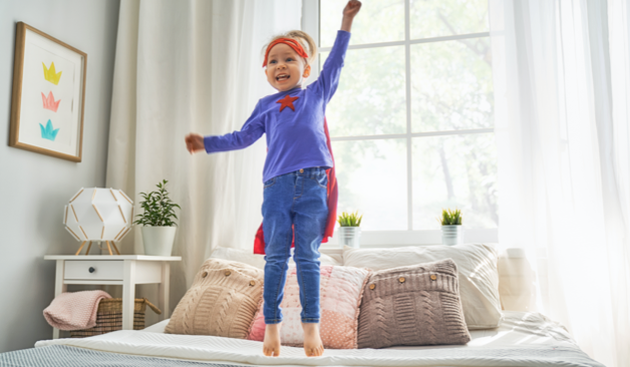 Young child dressed as a superhero playing on the bed